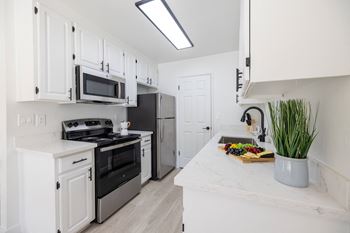 A kitchen with white cabinets and stainless steel appliances and a counter top with a sink